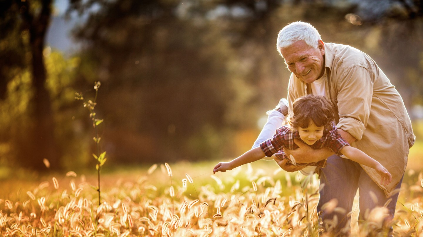 Grandfather holding smiling young boy over wheat field