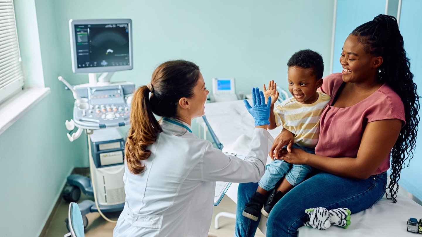 Mother and young son giving doctor high five in emergency department room